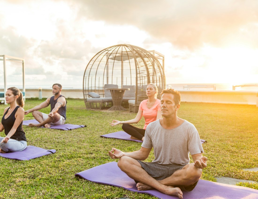 Group meditating outdoors on yoga mats